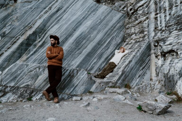 Two fashion models in sweaters pose against a rocky backdrop.